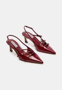 Tacchi slingback in vernice rossa con punta affusolata e cinturini sottili, dotati di accenti in metallo color oro. Design elegante e minimalista.