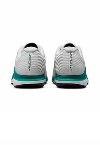 Scarpe da ginnastica bianche con superficie texturizzata, dotate di un accento turchese sulla suola e sul marchio. La vista posteriore mostra un design del tallone curvo.