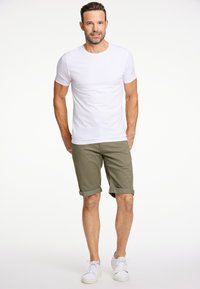 T-shirt bianco con colletto a girocostato, pantaloni corti verde oliva con risvolto e sneakers bianche indossati da una figura maschile su uno sfondo semplice.