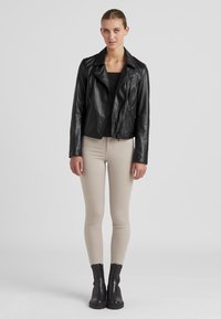 Schwarze Leder-Motorradjacke mit Reißverschluss, schmal geschnittene beige Hose und schwarze Stiefeletten. Glatte Textur und klassische Designdetails.