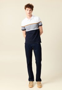 Marinblå och vit färgblockerad polo med grå rand, korta ärmar och ljusbruna accenter. Kombinerad med mörkblå jeans och ljusbruna skor.