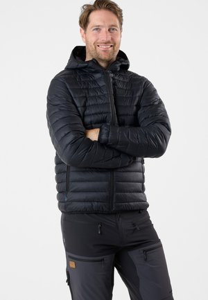 Schwarze gepolsterte Jacke mit Kapuze, ausgestattet mit horizontalem Steppdesign und frontaler Reißverschlussreihe. Getragen mit grauen Hosen, die Taschen zeigen.