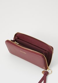 Burgundy leather wallet with gold zipper, featuring multiple compartments and a wrist strap. Inside is smooth and unembellished.