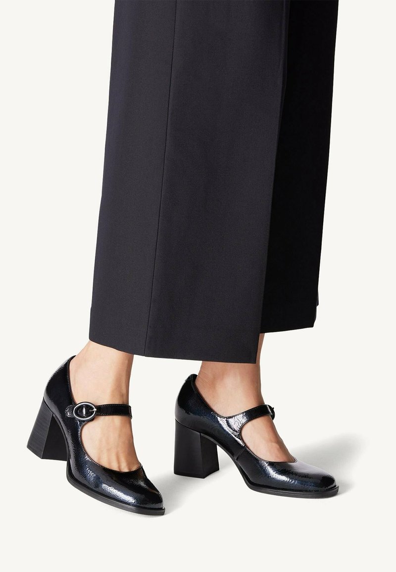 Escarpins Mary Jane en cuir verni noir avec un bout rond, un talon carré chunky et une sangle ajustable dotée d'une boucle en métal circulaire.