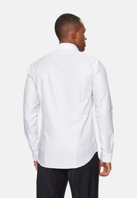 Camisa blanca de manga larga con un patrón sutil, hecha de una tela ligera. Presenta un collar estándar y puños abotonados.