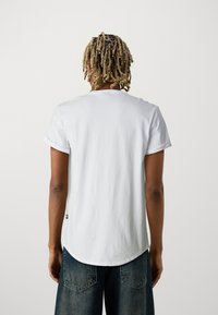 Vit bomullströja med korta uppvikta ärmar, rund halsringning och en böjd nederkant. Kombineras med mörka jeans med bakfickor.