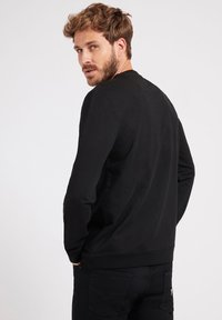 Svart langermet genser laget av bomull, med rund hals og tettsittende design, båret med mørke jeans. Bakfra fremhever den glatte teksturen.