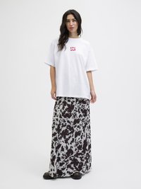 Biała, oversize koszulka z czerwonym napisem "STAY WILD", w zestawieniu z długą, zwiewną spódnicą w czarno-białe wzory oraz czarnymi butami.
