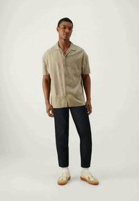 Short-sleeve, light gray button-up shirt with a relaxed fit, paired with dark trousers and cream sneakers featuring brown soles.