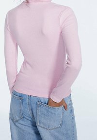 Světle růžový žebrovaný dlouhý rukáv s vysokým límcem, doplněný o světle modré mírně volné džíny s kapsami vzadu.