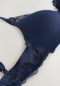 Soutien-gorge bleu marine avec des bonnets matelassés, présentant des bordures en dentelle et des bords festonnés. Tissu lisse avec des accentuations en dentelle décoratives sur les côtés.