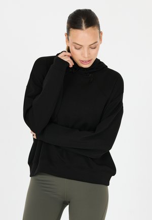 Sweat à capuche noir en matériau doux, doté de manches raglan et d'un cordon de serrage. Assorti à un legging vert olive.