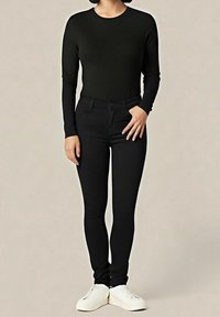 Haut noir à manches longues et pantalon noir slim en tissu stretch, associés à des baskets blanches. Design simple, ajusté, sans ornements.