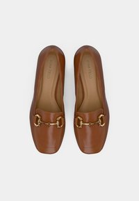 Mocassins en cuir marron avec un bout carré, ornés d'une chaîne dorée et d'une texture lisse, marqués "ANNA FIELD" sur la semelle intérieure.