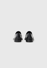 Scarpe in pelle nera con una texture liscia, design a profilo basso, stile slip-on e dettagli di cucitura minimi sulla tomaia.