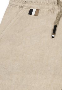 Pantaloni corti in lino beige con vita elastica, dotati di un'etichetta decorativa multicolore e un cordino con dettagli neri.
