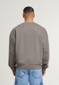 Sweatshirt gris surdimensionné avec un col et des poignets côtelés, texture douce et épaules tombantes, associé à un pantalon cargo bleu clair.
