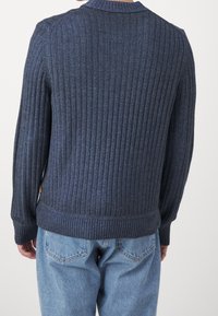 Granatowy sweter z prążkowanej dzianiny, z okrągłym kołnierzykiem, dopasowanymi mankietami i prostym dołem. Teksturowana tkanina z subtelnymi tonalnymi wariacjami.