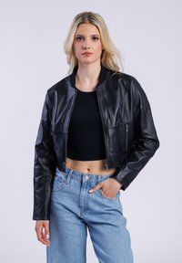 Černá kožená zkrácená bunda se zipem vpředu, žebrovaným límcem a dvěma bočními kapsami, v kombinaci s džíny z modrého denimu s vysokým pasem.