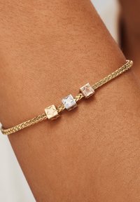 Bracelet tressé en or avec trois accents carrés en or jaune, argent et or rose, chacun présentant un motif d'étoile. Texture lisse.