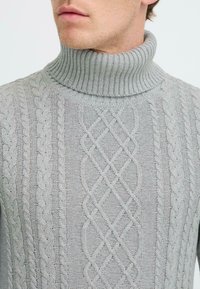 Lys grå turtleneck genser med ribbet krage og teksturerte kabelstrikkmønstre, med en jevn og myk stofffinish.