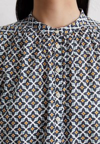 Kragenhemd aus Baumwolle mit geometrischem Muster in Marineblau, Orange und Hellblau auf weißem Hintergrund, mit weißen Knöpfen.
