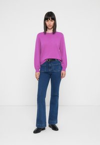 Lilla strikkegenser med lange ermer, parret med blå utsvingte jeans med baklommer. Svart ankelstøvler fullfører antrekket.
