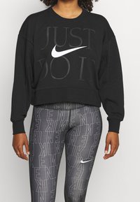 Sweat-shirt court noir avec le texte en relief « JUST DO IT » et un logo Nike blanc. Associé à des leggings gris présentant un motif Nike répété.