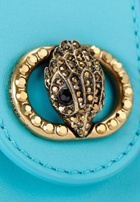 Pelle turchese con una chiusura in tono oro caratterizzata da un design decorativo di una mano adornata con embellishments neri e dorati.