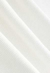 Tessuto bianco testurizzato con motivo a griglia in rilievo, che mostra una sottile dimensionalità e un aspetto liscio, drappeggiato diagonalmente.