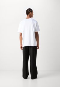 Vit kortärmad t-shirt i kombination med lösa svarta byxor, sedd bakifrån. Tyget ser slätt och lätt ut.