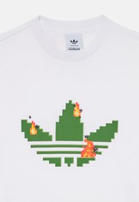 Camiseta de algodón blanca con un logo de Adidas pixelado en verde y llamas en rojo y naranja. El diseño incluye tres rayas horizontales verdes debajo del logo.