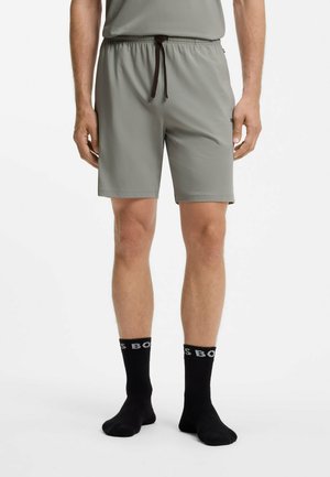 Man draagt lichtgrijze shorts met elastische taille, zwarte trekkoord en zwarte kniekousen met witte letters op een witte achtergrond.