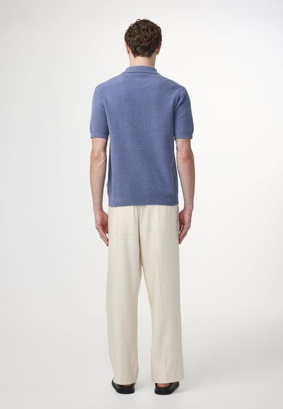 Kurzärmliges, hellblaues Poloshirt mit strukturiertem Strickfinish, kombiniert mit cremefarbenen, weit geschnittenen Hosen und schwarzen flachen Schuhen.