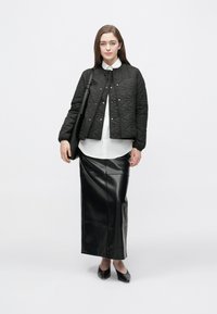 Jachetă neagră matlasată cu nasturi tip capse, cămașă albă cu nasturi, fustă neagră din piele, mulată, și pantofi negri cu vârf ascuțit.