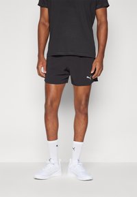 Svarta sportshorts tillverkade av lättviktsmaterial, med en liten vit logotyp. Matchas med en svart t-shirt och vita sneakers.