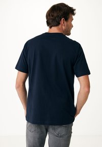 Marinblå t-shirt med korta ärmar, rund halsringning och en slät textur. Bärs med grå jeans, visande bakifrån.