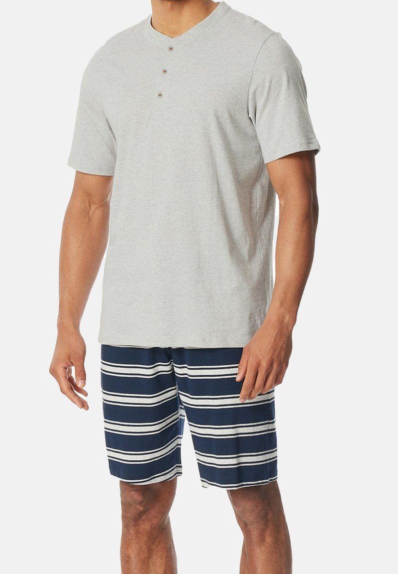 Camiseta henley de manga corta gris con tres botones; combinada con pantalones cortos de baño azul marino con rayas blancas horizontales y un ajuste relajado.