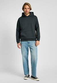 Sudadera con capucha de color gris oscuro, con un bolsillo frontal, combinada con jeans de color azul claro y zapatillas negras, presenta un ajuste casual y una textura suave.