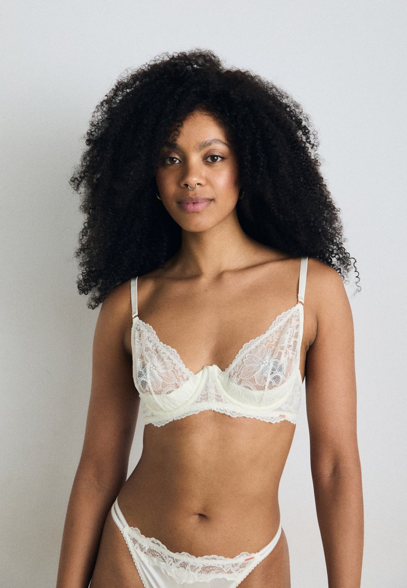 Lace bralette and matching panties in light cream. The bralette features semi-transparent lace cups with scalloped edges and thin straps.