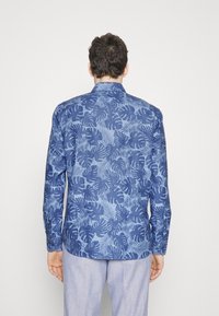 Blå knapp-up skjorta med lövmönster, tillverkad av lättviktsmaterial, långa ärmar och rundad nedkant. Bakifrån visad.