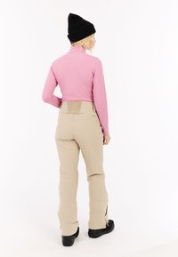 Šviesiai rožinė ilgomis rankovėmis palaidinė, derinama su smėlio spalvos kelnėmis, turinčiomis tekstūruotą nugaros panelę ir užtrauktukus ant kulkšnies. Juoda megzta kepurė papildo šį įvaizdį.