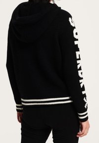 Felpa nera con cappuccio caratterizzata da un marchio bianco sulla manica, materiale in maglia testurizzata e polsini a coste con strisce bianche all'orlo.