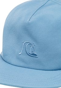 Gorra de tela azul con visera plana y logo de ola bordado. Presenta un material texturizado y duradero así como una construcción sin costuras.