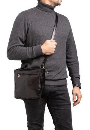 Sac à épaule en cuir noir avec une texture lisse, forme rectangulaire, bandoulière ajustable et une poche zippée à l'avant. Positionné sur un fond uni.