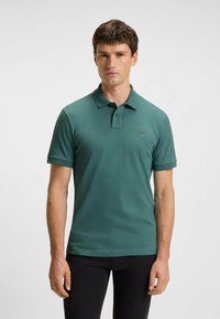 Polo verde realizzato in tessuto morbido, con colletto, una pattina con due bottoni e un piccolo logo sul petto. Maniche corte.