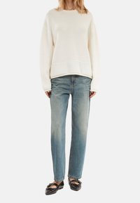 Sweat-shirt couleur crème avec une coupe décontractée, doté d'un col et d'un bas côtelés. Associé à un jean droit bleu clair légèrement délavé et des ballerines noires.