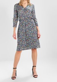 Kukkaprintti mekko, jossa on kolmanneksen hihat, V-pääntie, joustava vyötärö ja polvipituinen helma. Valmistettu kevyestä kankaasta, sisältää värikkäitä kuvioita.