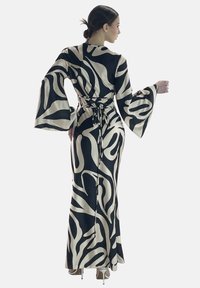 Robe longue avec des manches évasées dans un motif abstrait noir et ivoire, dotée d'une taille cintrée avec des liens et d'une silhouette fluide. Texture lisse.