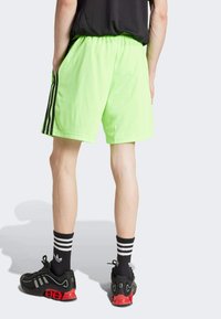 Neon green athletic shorts with an elastic waistband and black side stripes, paired with black shoes featuring red accents and striped socks.
